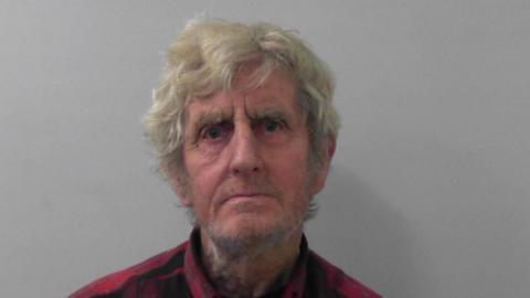 A police mugshot of Herning Thompson, who has mid-length white hair. He wears a neutral expression in the photo.