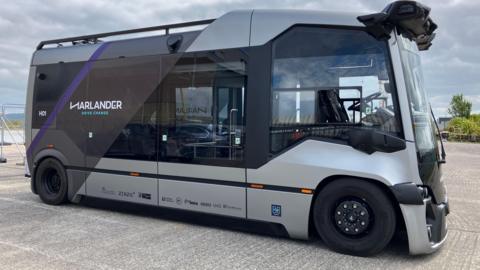 A small silver bus that has the branding 'Harlander' on the side.