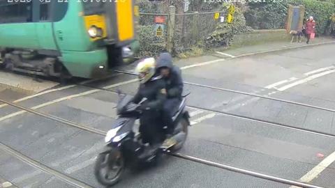 Two people on a moped narrowly escape being hit by a train