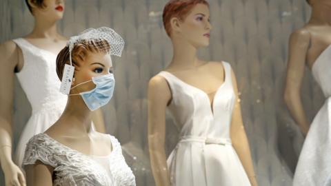 Brides dresses on mannequins with one wearing a surgical mask