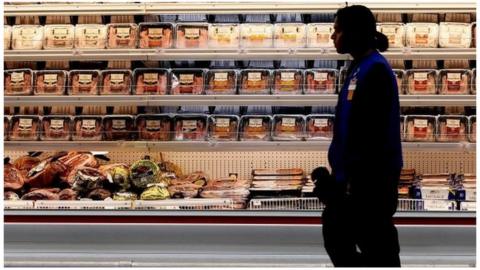 A employee walks by a meat cooler in the grocery section of a Sam"s Club during a media tour in Bentonville, Arkansas, U.S. on June 5, 2014