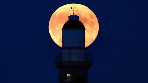 The full Moon behind a lighthouse
