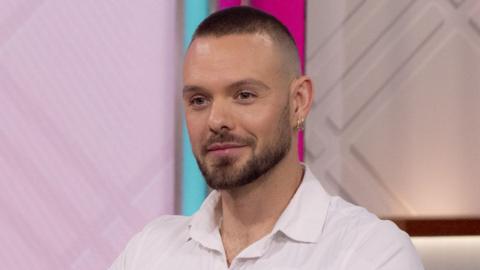 John Whaite pictured on ITV's Lorraine in August 2023, wearing a white shirt and looking straight ahead