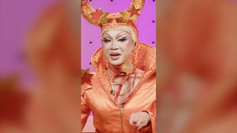 Gawdland is wearing an orange had with horns and an orange top