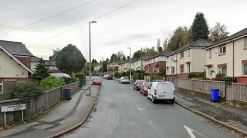 Houses are either side of a road. A sign on the left hand side says Summerville Road. There are seven cars parked along the road, along with a van.