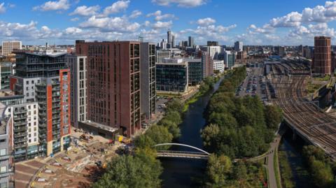 Aerial panorama of Leeds city centre skyline with River Aire, modern high-rises, and railway tracks in Yorkshire, England.