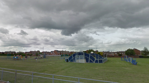 View of blue and grey-coloured play equipment at the park, with grass and metal railing in the foreground