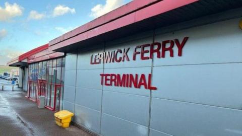 Lerwick Ferry Terminal building - sign in red block capital letters, a yellow bin is visible, and cars in distance