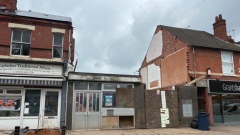 A partially demolished building in between two shops