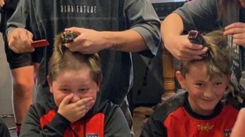 A pair of young boys giggle as two adults start to shave their hair off