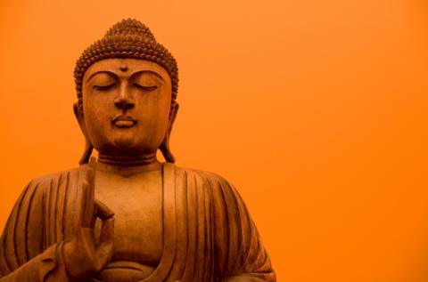 A wooden carving of Buddha against an orange background