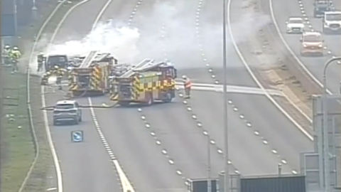 Traffic camera view of the motorway, with two fire appliances beside a van-type vehicle from which smoke is billowing