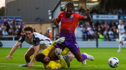Garath McCleary goes down under a challenge from Bromley goalkeeper Grant Smith, who is lying on the floor with McCleary's knee in his face and the ball away to the right