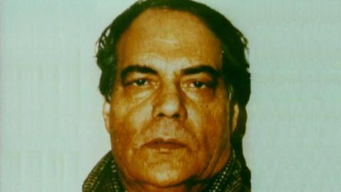 A police mugshot of Muhammed Saeed. He has dark hair and is wearing a tweed jacket.