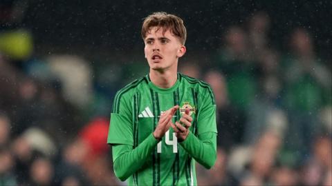 Isaac Price looks out to the crowd and claps wearing a green northern ireland kit