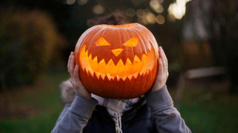 Person holding a carved pumpkin in front of their face