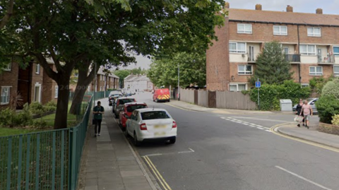 Blocks of flats and terraced houses line Fyning Street and Charles Street which form a T-junction near a small fenced garden.
