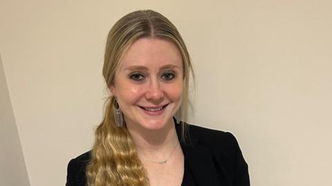 Melanie, a woman with golden shoulder-length hair, wearing a black shirt, smiling for camera.