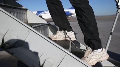 A Honduran immigration detainee, his feet shackled and shoes laceless as a security precaution, boards a deportation flight to Honduras