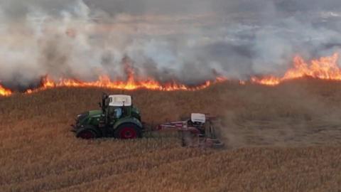 A tractor attempts to make a fire break while fire burns in the background