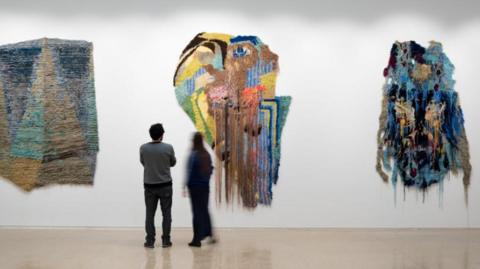 A photo of two people looking at artwork on a wall, which looks like a smear of coloured paint.