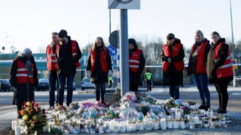 People stand next to candles and flowers placed near the Risbergska school