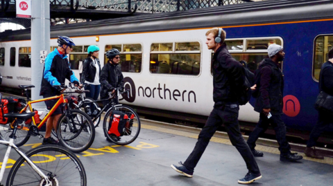 Passengers walk in front of a Northern train