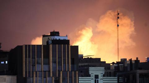 Smoke and flames rise behind buildings after an explosion on the second consecutive day of strikes by the US and Israel, in Tehran, Iran, 01 March 2026.