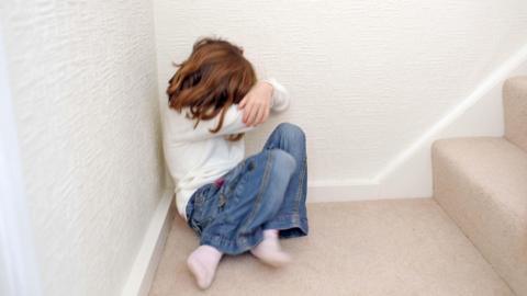 Stock image of a young girl (6 years of age) sits on the landing of a staircase (stairs) and covers her face.