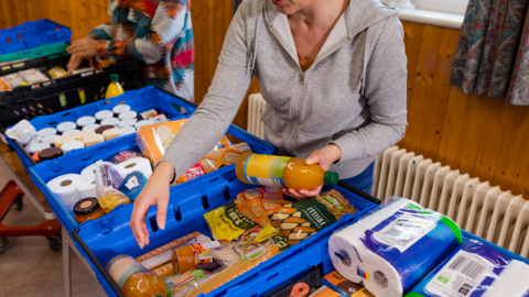 A woman in a grey top reaching into blue boxes of food at a foodbank