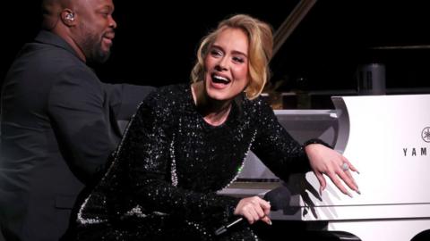 Adele sat on a piano bench with a pianist