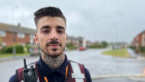 Community safety warden Bradley Ellis in his uniform. He has a neck tattoo and several piercings