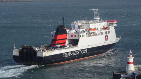 A large black and white ship with a red funnel and Steam-Packet.Com written on the side sails away from the camera. 