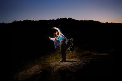A dancer performs in a spotlight. The rest of the image is dark. 