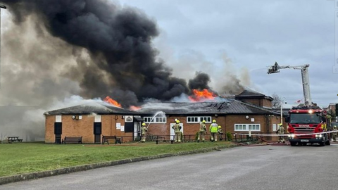 A photograph of the village hall on fire with firefighters attempting to extinguish the flames.