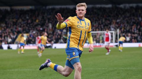 Mansfield forward Will Evans runs on the pitch and holds his right arm up