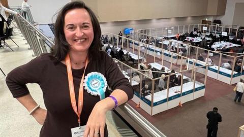 Woman with brown hair and a brown top wearing a Reform UK rosette