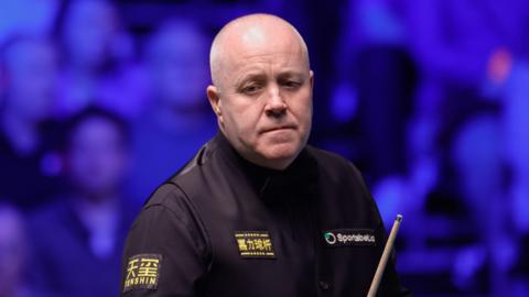 John Higgins holding a cue at the Tour Championship 