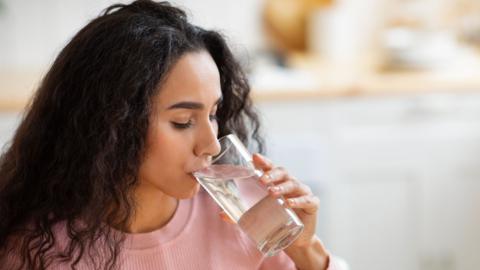 A woman takes a sip from a glass of water.