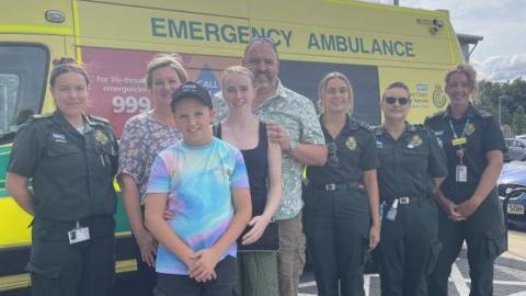 Giles, his family and paramedics stand in front of an ambulance