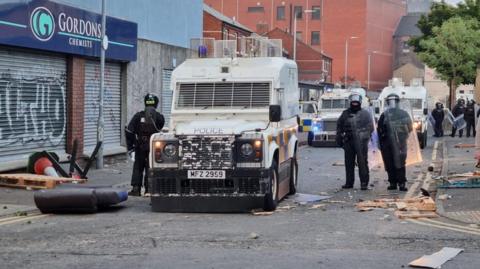 Police in riot gear stand guard in rubbish-strewn street