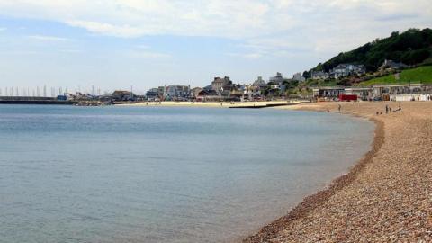 Lyme Regis front beach - a shingle beach to the right with the sea to the left and buildings in the distance.