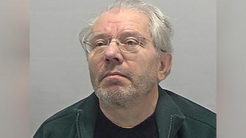 David Marriott wearing a green zipped fleece and a black T-shirt and round-rimmed glasses.