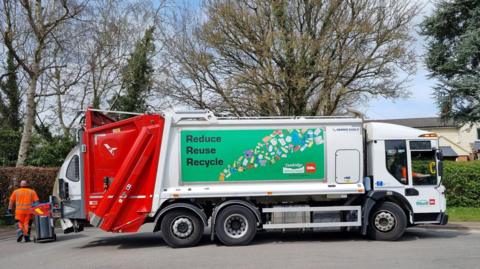 A Biffa recycling lorry is parked on a residential street beside wheelie bins. The vehicle displays a large "Reduce Reuse Recycle" sign and branding from Tandridge District Council and Biffa, with collection staff visible nearby.
