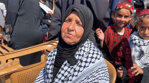Safia Qeshta sat in a chair. She has a black hijab and is next to two young girls