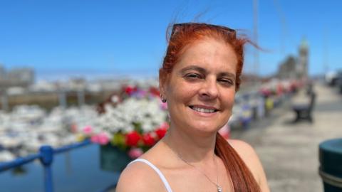 A woman with orange hair smiling sitting in front of a marina. 