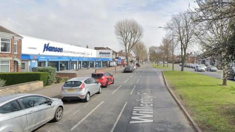 A Google Streetview picture of Willerby Road, with the Hanson Electrical shop on the left and a grassy central reservation lined with trees