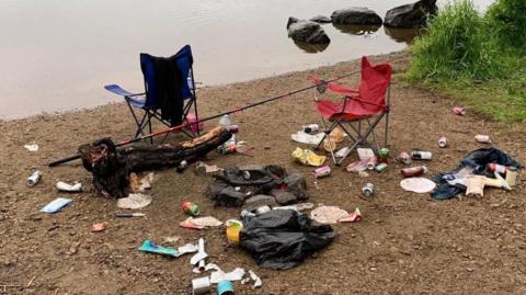 A heap of rubbish and abandoned camping chairs next to a loch