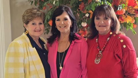 Denise, Maureen and Anne Nolan posing together on front of an autumnal tree