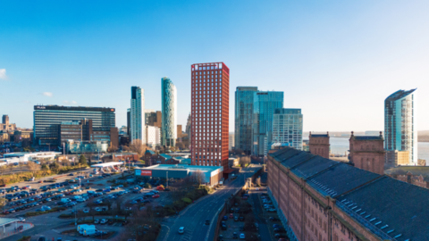 Image shows a planned 28-storey tower block to be built near Liverpool's Three Graces. The image shows the view from the Waterloo Warehouse, a long red-brick 19th century building. A number of tall buildings obscure the view of the waterfront. 